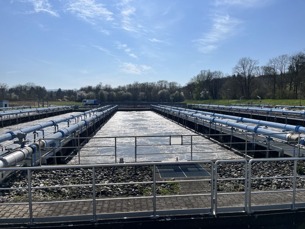 Rechteckiges Klärbecken der Kläranlage Reutlingen-West bei blauem Himmel im Hintergrund.