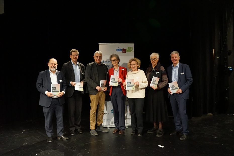 In der Mitte vor einem bunten Roll-Up: Projektleitung und regionale Partner:innen präsentieren den Entwurf der Abschlussbroschüre mit 18 Empfehlungen: V. l. n. r.: Prof. Dr. Stephan Seiter, Dr.-Ing. Volker Kienzlen, Arne Braun, Prof. Dr. Sabine Löbbe, Angela Weiskopf, Gudrun Heute-Bluhm, Prof. Dr.-Ing. Bernd Thomas.