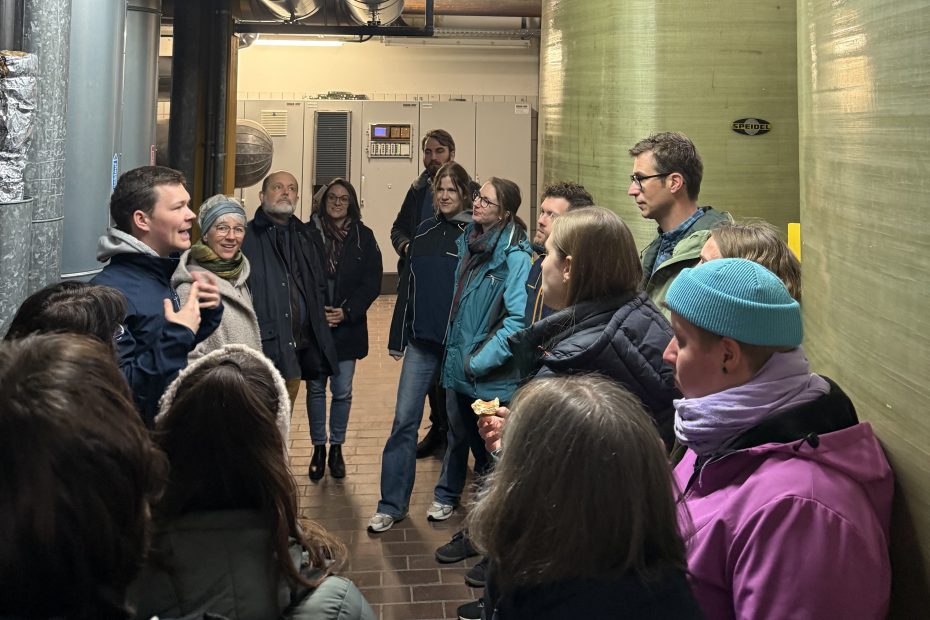 Gruppe von 15 Personen steht vor zwei gelben Heizkesseln, rechts im Hintergrund. Philipp Häberer führt durch Heizräume und Abfallsysteme.
